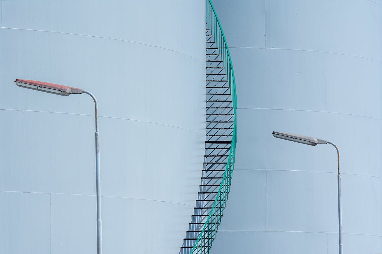 Minimalist view of industrial tanks with a staircase and lampposts.